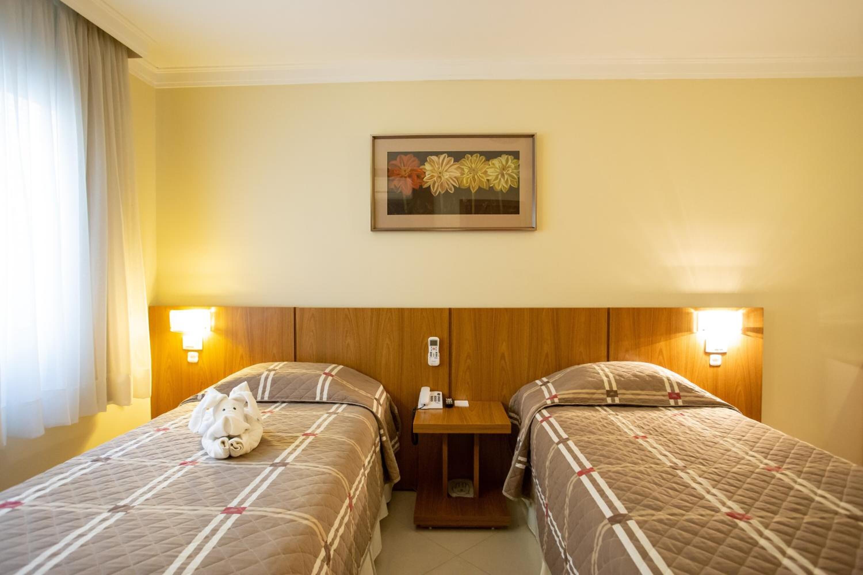 A hotel room with two beds, a wooden headboard, bedside lamps, a small table, and a framed picture on the wall.
