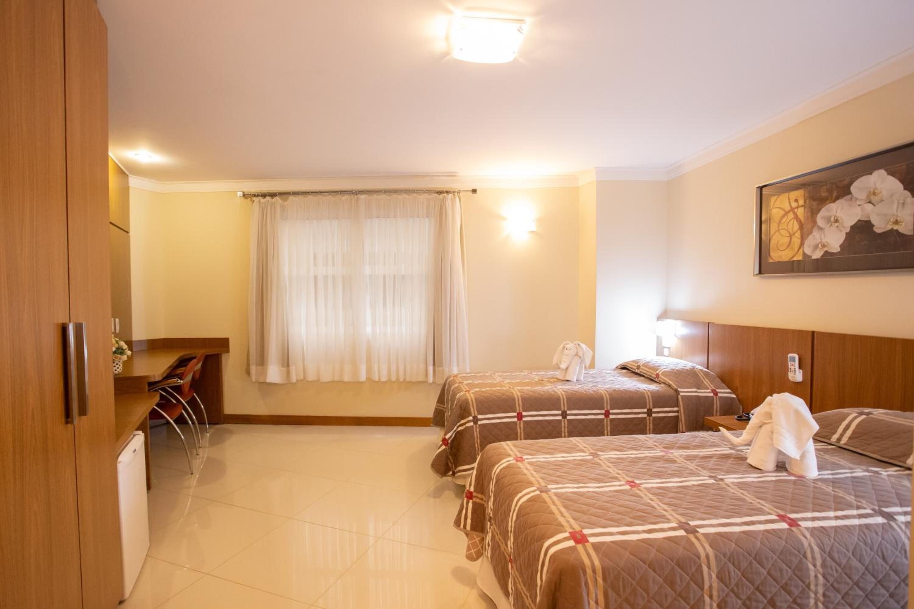 A hotel room with two beds, a desk, a chair, and a small refrigerator.