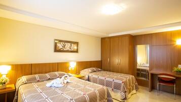 A hotel room with two beds, a desk, and a chair. There is a framed picture on the wall and a lamp on the nightstand.