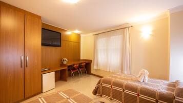 A hotel room with two beds, a TV, a desk, and a small refrigerator.