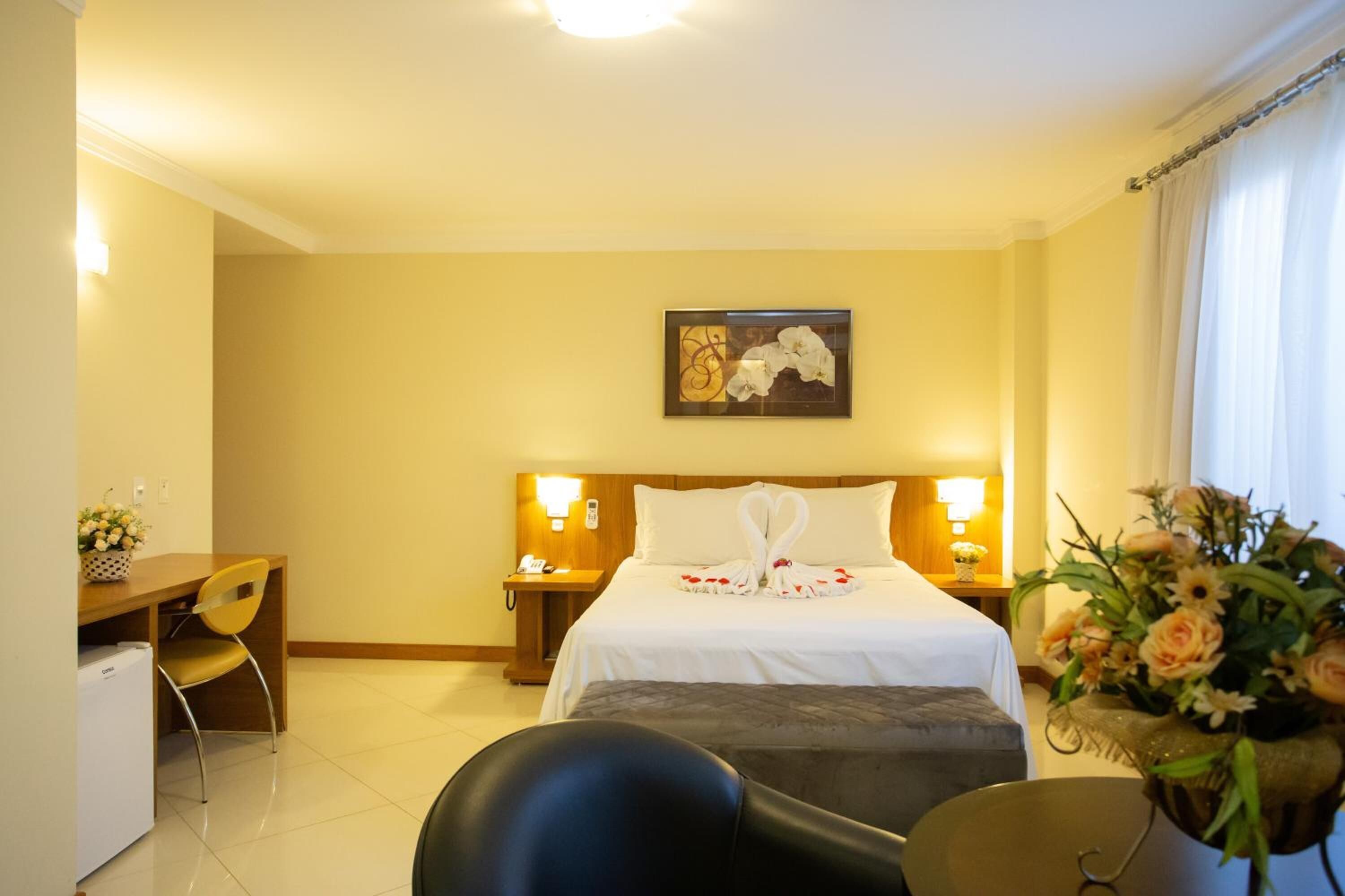 Habitación de hotel con cama, escritorio, silla, mesita de noche y un cuadro colgado en la pared.