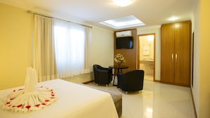 A hotel room with a bed, two chairs, a small table, a TV, and a wooden wardrobe. - Barbur Center Hotel (Ponta Grossa)