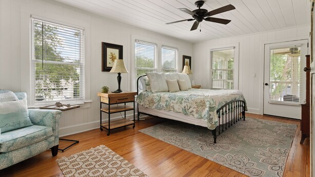 A bedroom with a bed, a nightstand, a lamp, a chair, and a ceiling fan. - Seventh Heaven Beach House on East Beach with Private Pool! (St Simons Island)