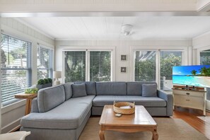 Een woonkamer met een grijze modulaire bank, een houten salontafel en een televisie waarop een strand te zien is.