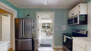 A compact kitchen with a stainless steel refrigerator, a microwave, and a stove. There is a door leading to a patio area with outdoor seating. - Seventh Heaven Beach House on East Beach with Private Pool! (St Simons Island)