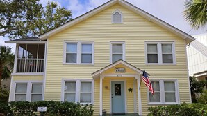 A yellow two-story building with a porch, a small flag, and a sign reading "7th Heaven" at the entrance. - Seventh Heaven Beach House on East Beach with Private Pool! (St Simons Island)