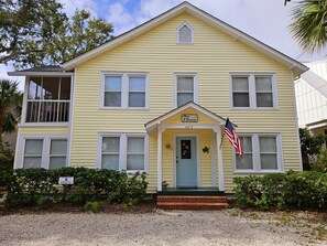 A yellow two-story building with a porch, a small flag, and a sign reading "7th Heaven" at the entrance. - Seventh Heaven Beach House on East Beach with Private Pool! (St Simons Island)