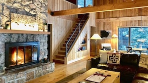 A cozy interior with a fireplace, wooden staircase, and a seating area with a coffee table. - Timber-frame Beach Chalet on Lake Superior between Lutsen and Grand Marais (Lutsen)