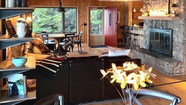 A cozy cabin interior with a dining area, kitchen, and stone fireplace. - Timber-frame Beach Chalet on Lake Superior between Lutsen and Grand Marais (Lutsen)