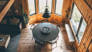 A wooden interior with a round table, chairs, a hanging light fixture, and large windows. - Timber-frame Beach Chalet on Lake Superior between Lutsen and Grand Marais (Lutsen)