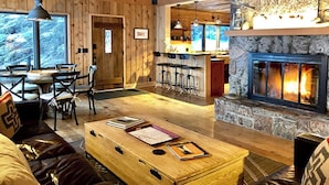 A cozy interior with a stone fireplace, wooden walls, a dining area with chairs, and a bar with stools. - Timber-frame Beach Chalet on Lake Superior between Lutsen and Grand Marais (Lutsen)