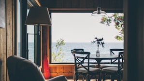 A room with a view of the sea, a dining table with chairs, a lamp, and a vase with flowers. - Timber-frame Beach Chalet on Lake Superior between Lutsen and Grand Marais (Lutsen)