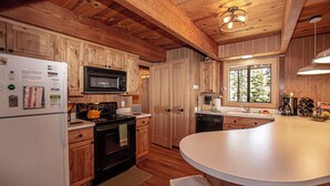 Une cuisine avec des meubles de rangement en bois, un réfrigérateur blanc, une cuisinière noire et un four à micro-ondes.