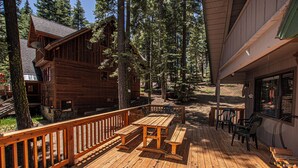 Une terrasse en bois, agrémentée de tables et de chaises pour pique-niquer, entourée d’arbres.