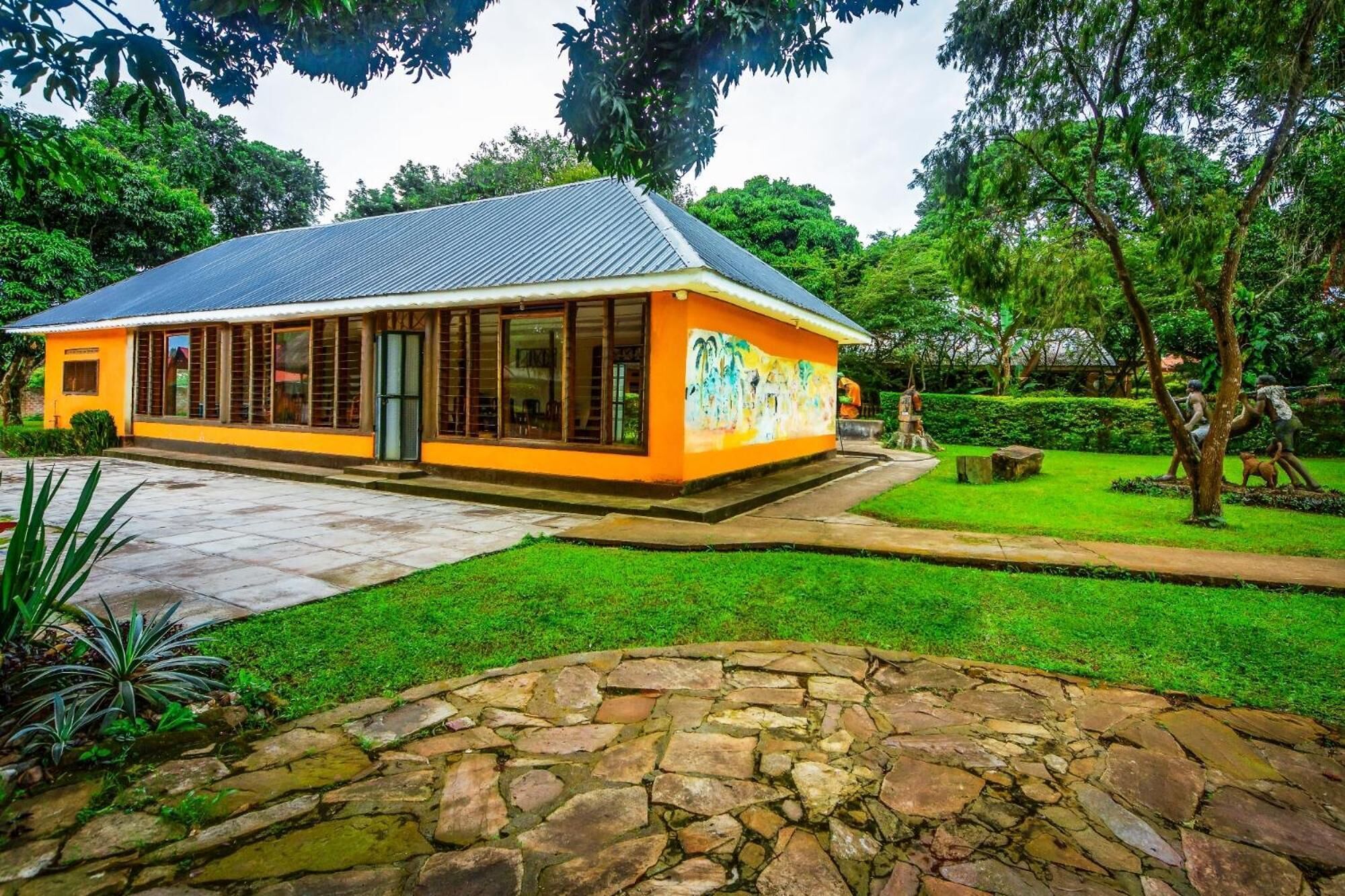 A building with a yellow exterior and a grey roof, surrounded by a well-maintained garden with a stone pathway leading to the entrance.