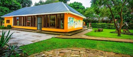 A building with a yellow exterior and a grey roof, surrounded by a well-maintained garden with a stone pathway leading to the entrance.