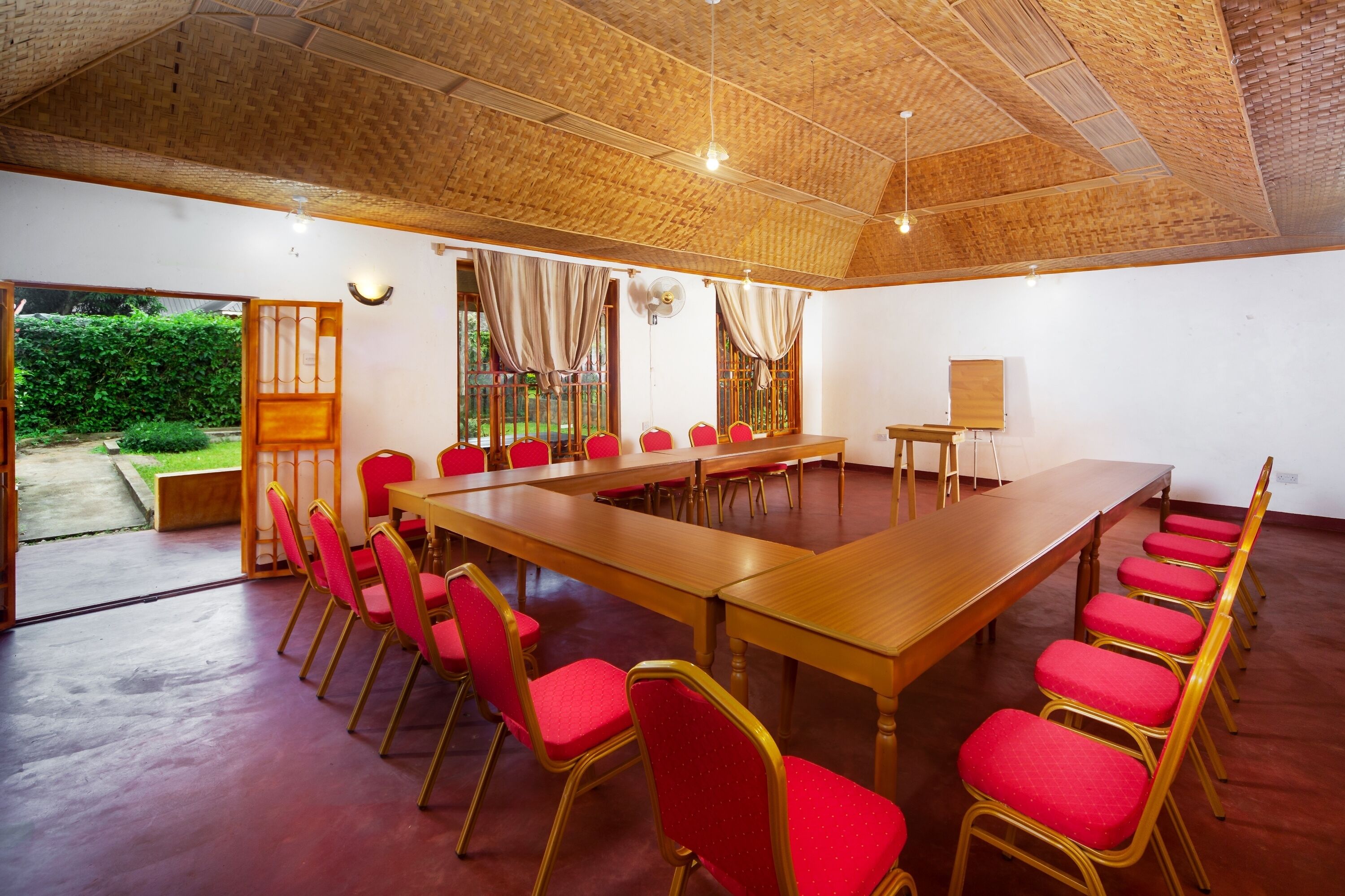 Sala de conferência com uma mesa comprida e cadeiras vermelhas, teto de madeira e vista para o verde lá fora.