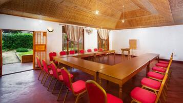 Sala de conferência com uma mesa comprida e cadeiras vermelhas, teto de madeira e vista para o verde lá fora.