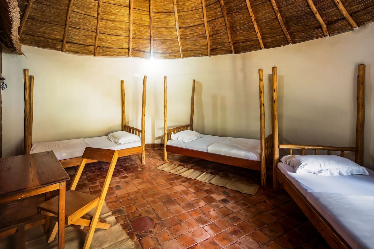 A rustic room with three wooden beds, a wooden table, and a thatched roof.