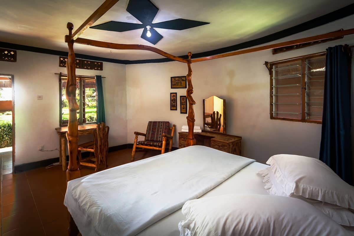 A room with a four-poster bed, a wooden desk, a chair, and a window with curtains.