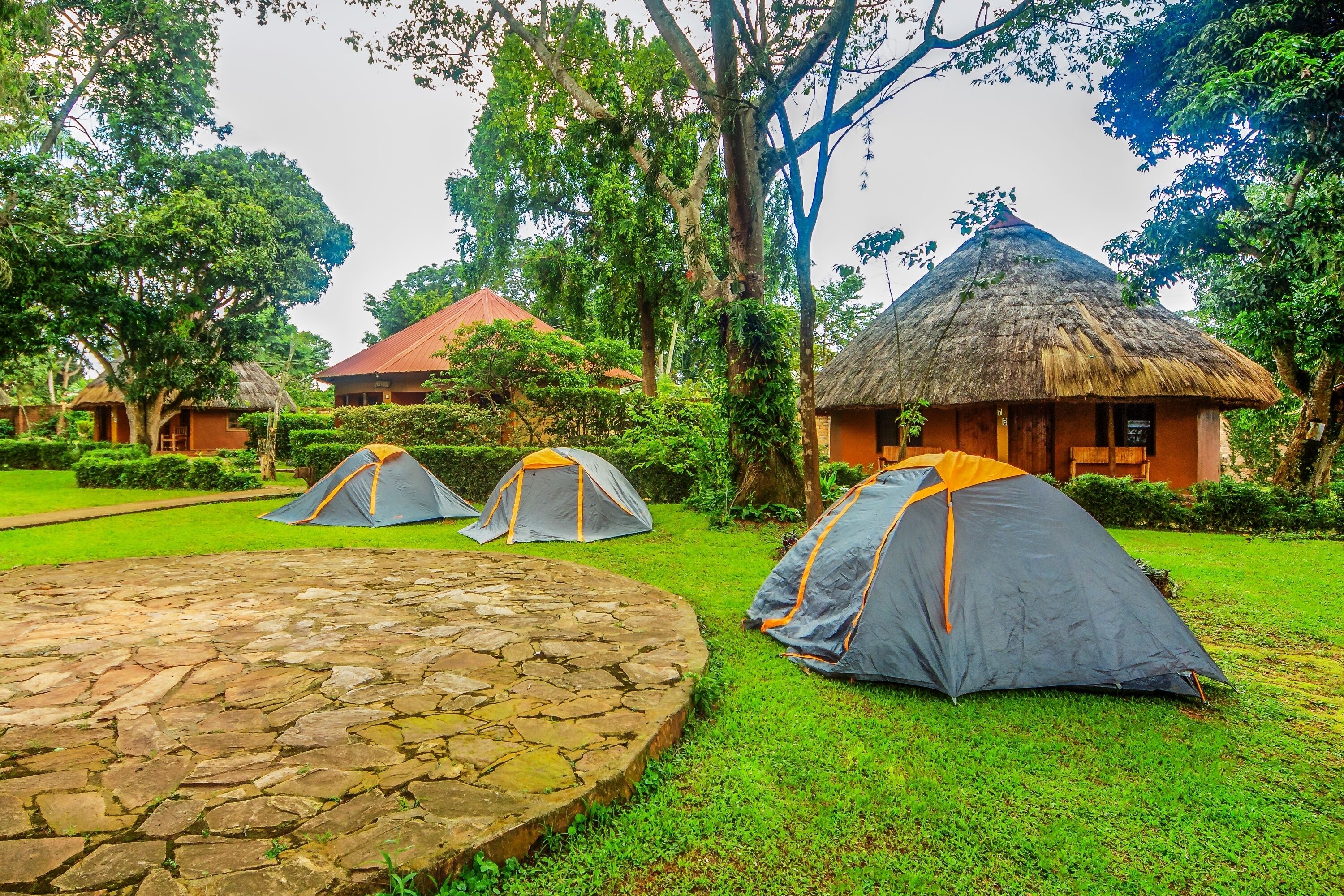 Un terrain de camping doté de huttes à toits de chaume, d’aires pavées de pierres et de tentes.