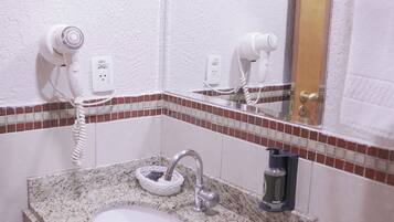 A bathroom with a granite countertop sink, a mirror, and two hair dryers mounted on the wall.