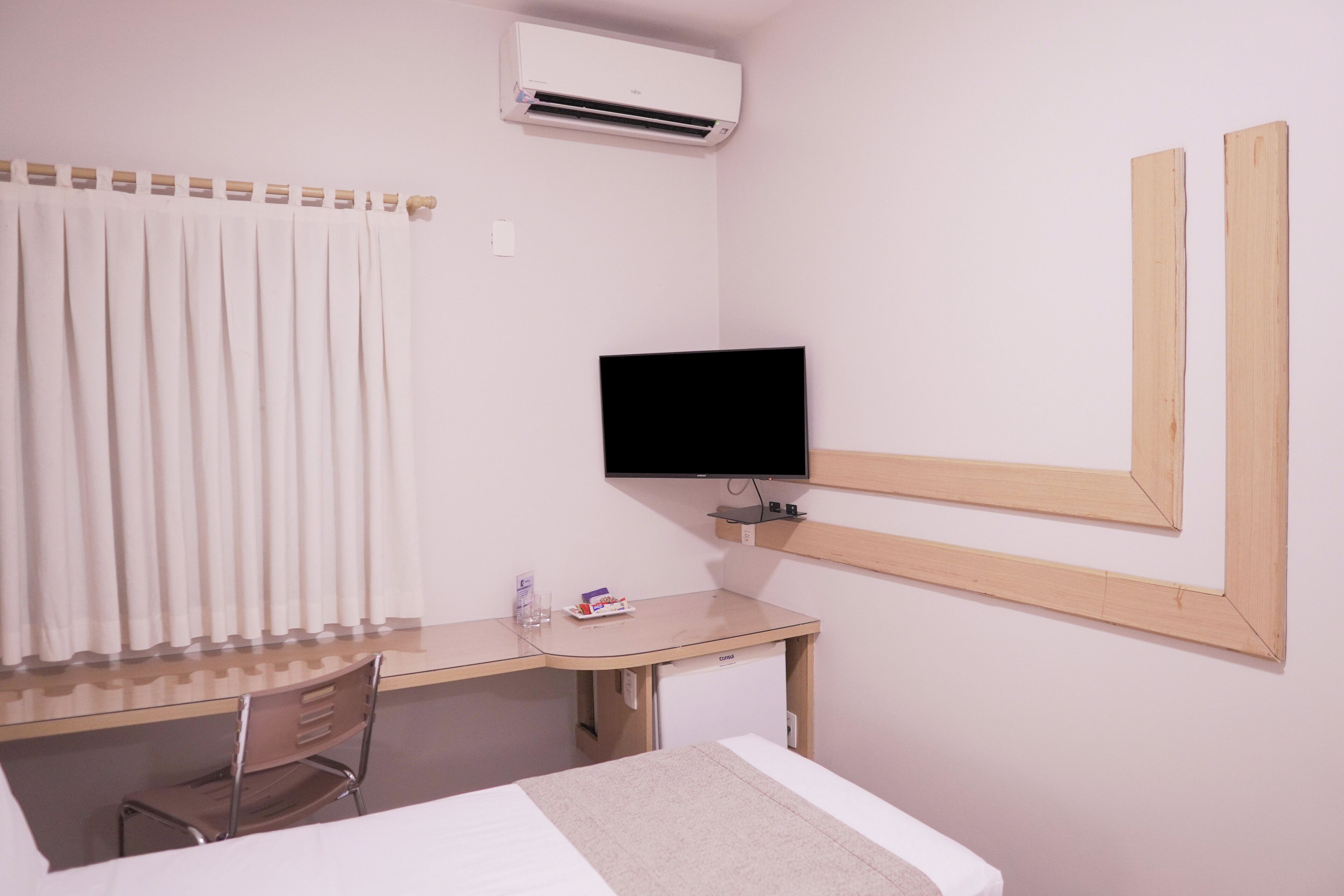 Una habitació d'hotel amb un llit, escriptori amb cadira, televisió i aire condicionat.