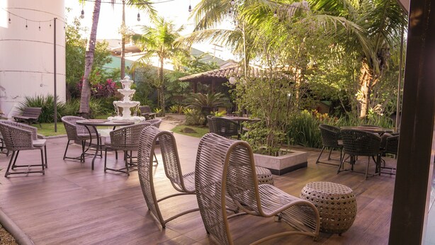 Un patio exterior con mobiliario de mimbre, una fuente y abundante follaje.