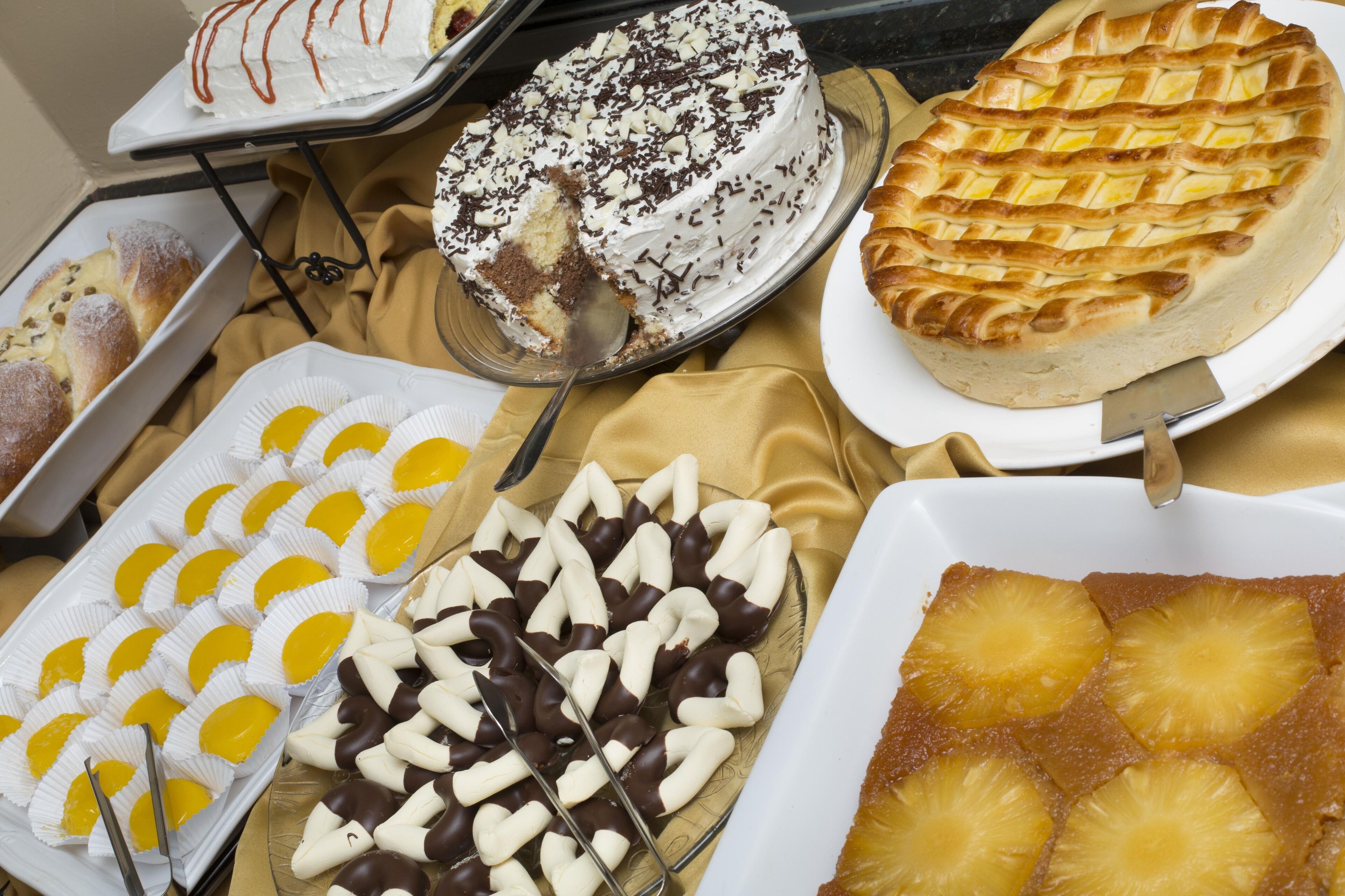 A variety of desserts on display, including a cake with white frosting and chocolate shavings, a pie with a lattice crust, and other sweet treats.