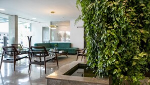 Una sala de estar moderna con un sofá verde, sillas de madera, una mesa de centro y una pared cubierta de plantas verdes.
