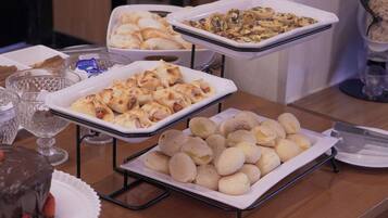 Uma mesa de buffet com diversos alimentos, incluindo pães, doces e uma sobremesa de chocolate.