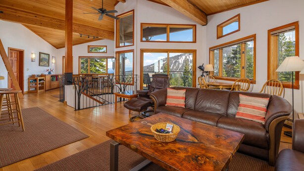 A spacious living area with a wooden ceiling, large windows offering mountain views, a leather sofa, and a dining area with a view.
