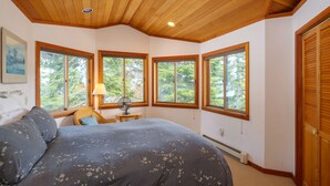 A bedroom with a large bed, multiple windows, a ceiling fan, and a nightstand.