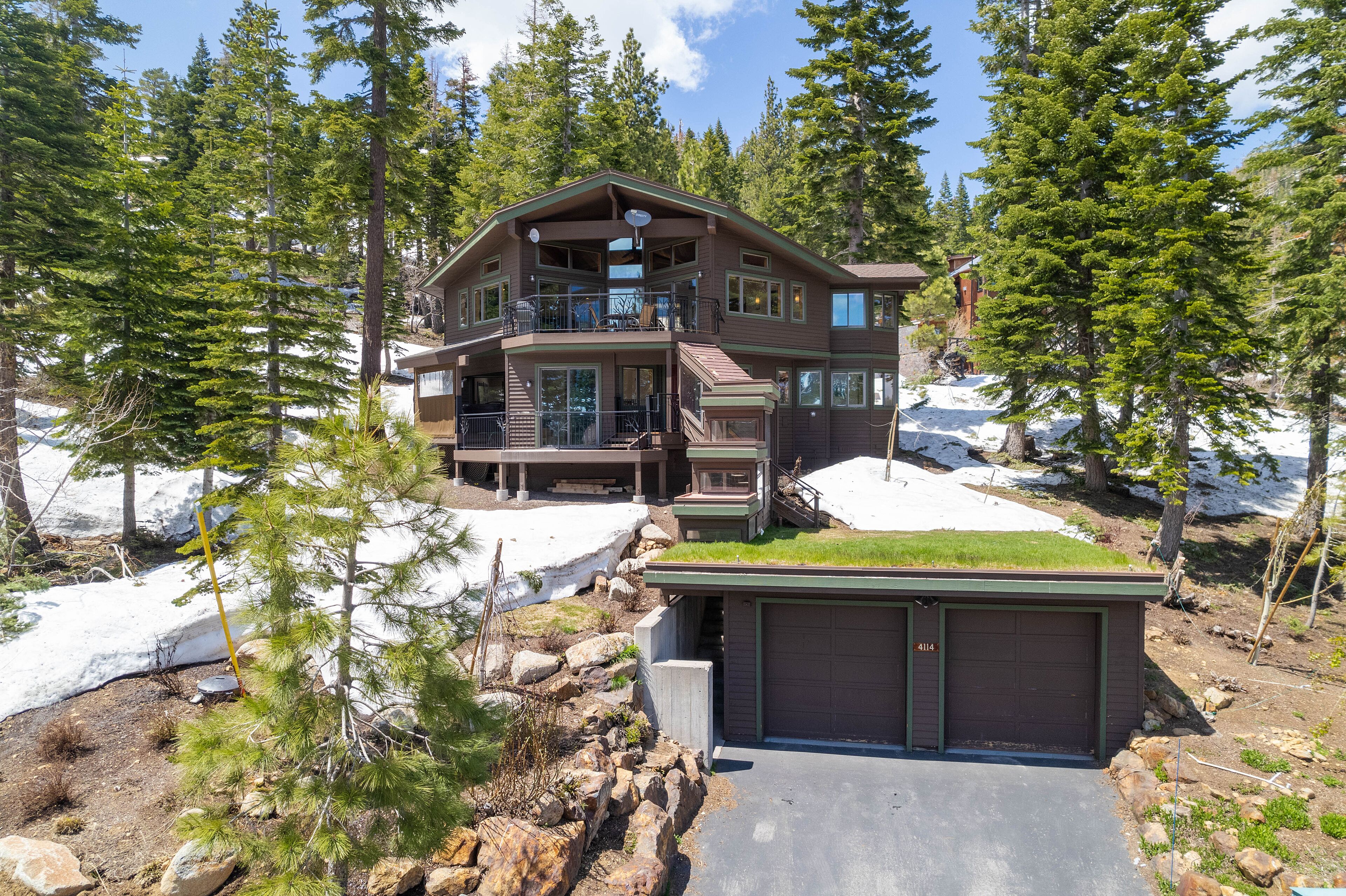 Une cabane en rondins à deux étages, dotée d’un balcon, entourée de neige et d’arbres.