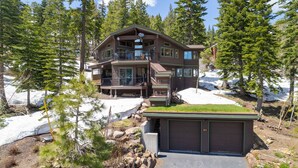 A two-story log cabin with a balcony, surrounded by snow and trees.