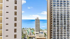 A high-rise hotel with multiple floors, a view of the ocean, and a distinctive building with a green roof in the background. - Bright ocean-view condo w/ lanai near the beach (Honolulu)