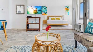 A hotel room with a bed, a television, a small table with a vase, and a sofa. - Bright ocean-view condo w/ lanai near the beach (Honolulu)