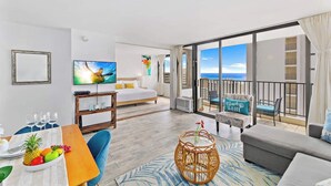 A hotel room with a bed, a TV, a dining table with fruit, a balcony with chairs, and a view of the sea. - Bright ocean-view condo w/ lanai near the beach (Honolulu)
