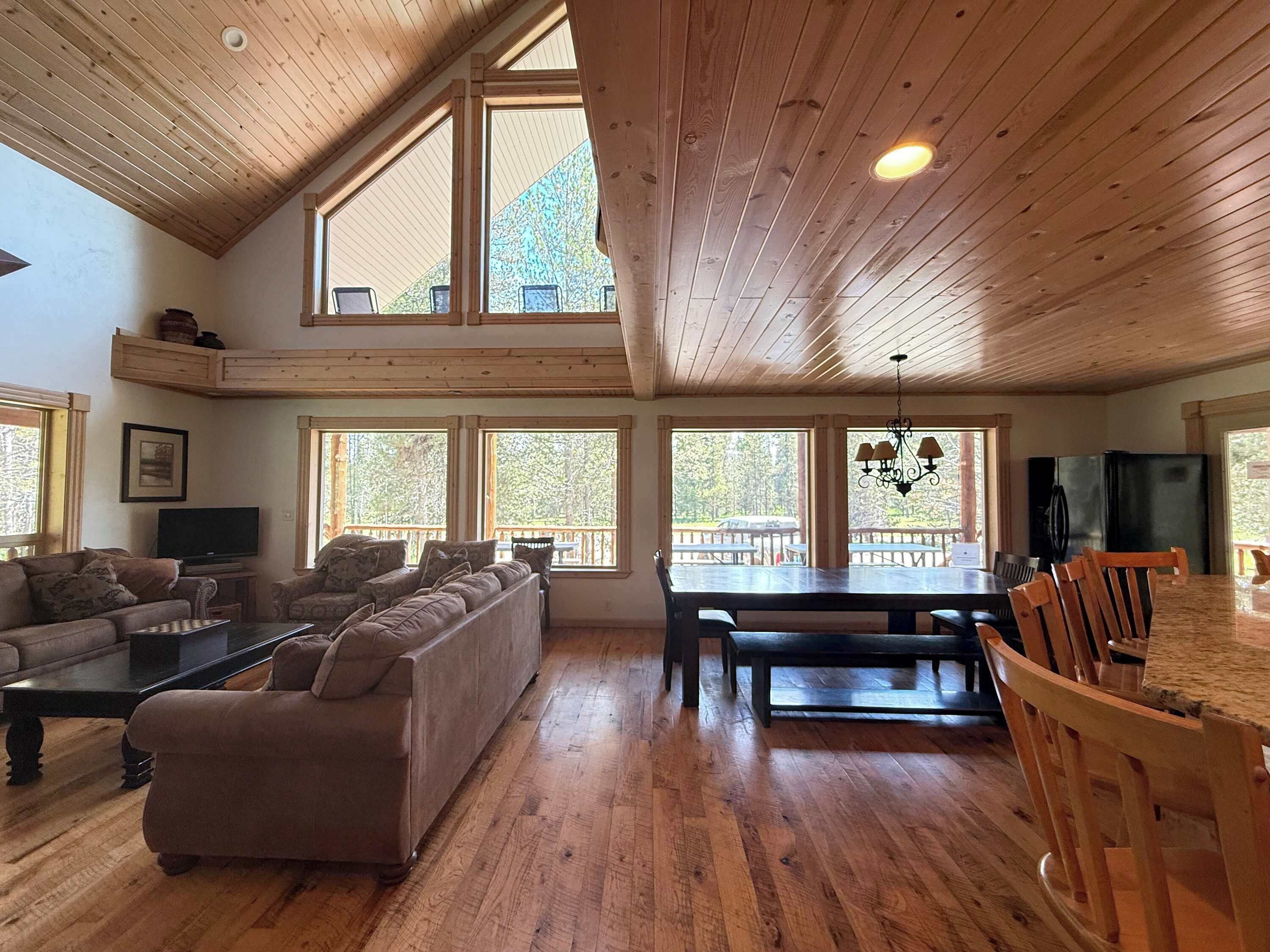 A spacious living area with a large sofa, a dining table, and multiple windows offering views of the outdoors.