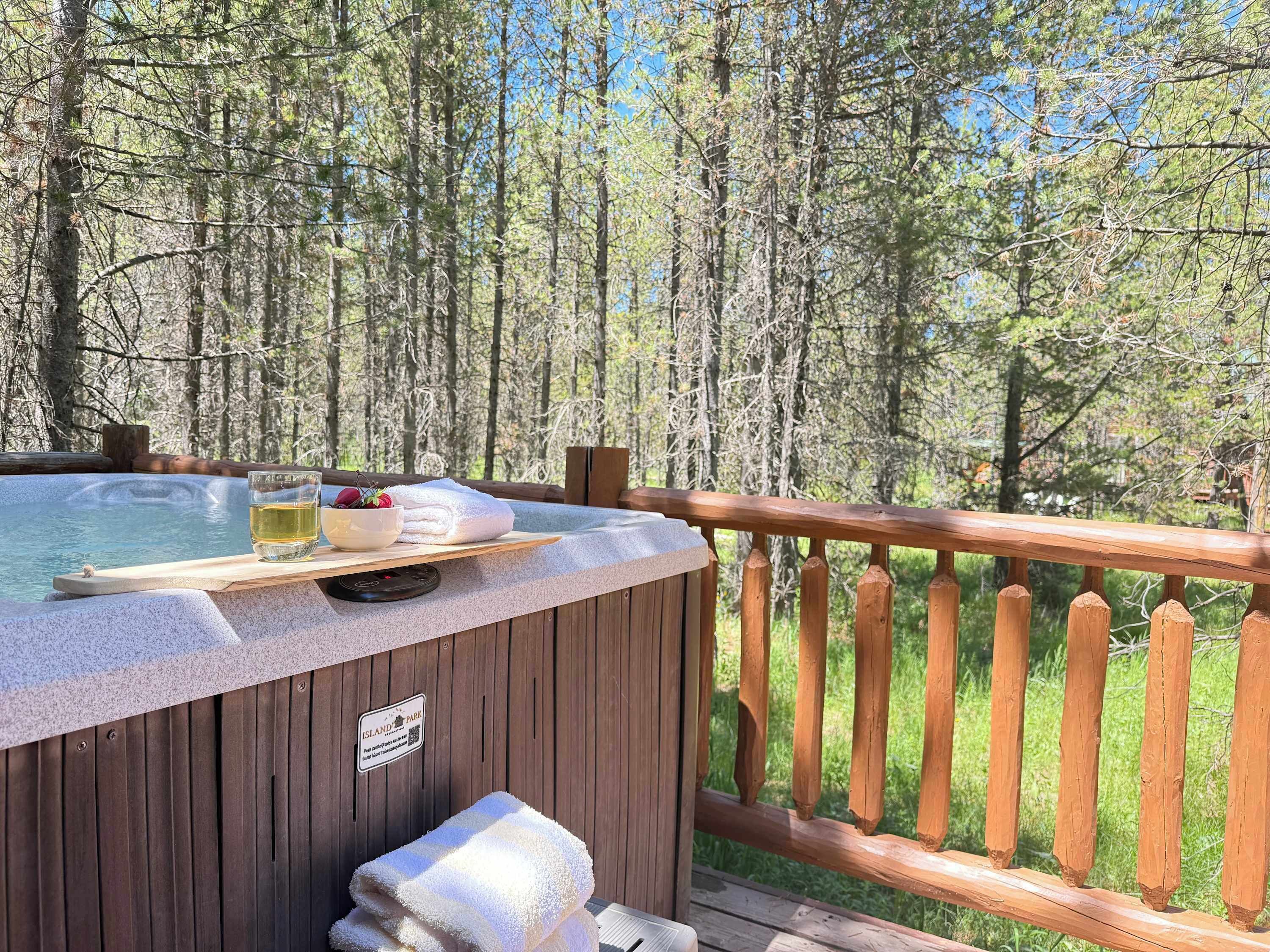 A hot tub with a wooden deck, surrounded by trees, and a sign indicating 'Island Park.'