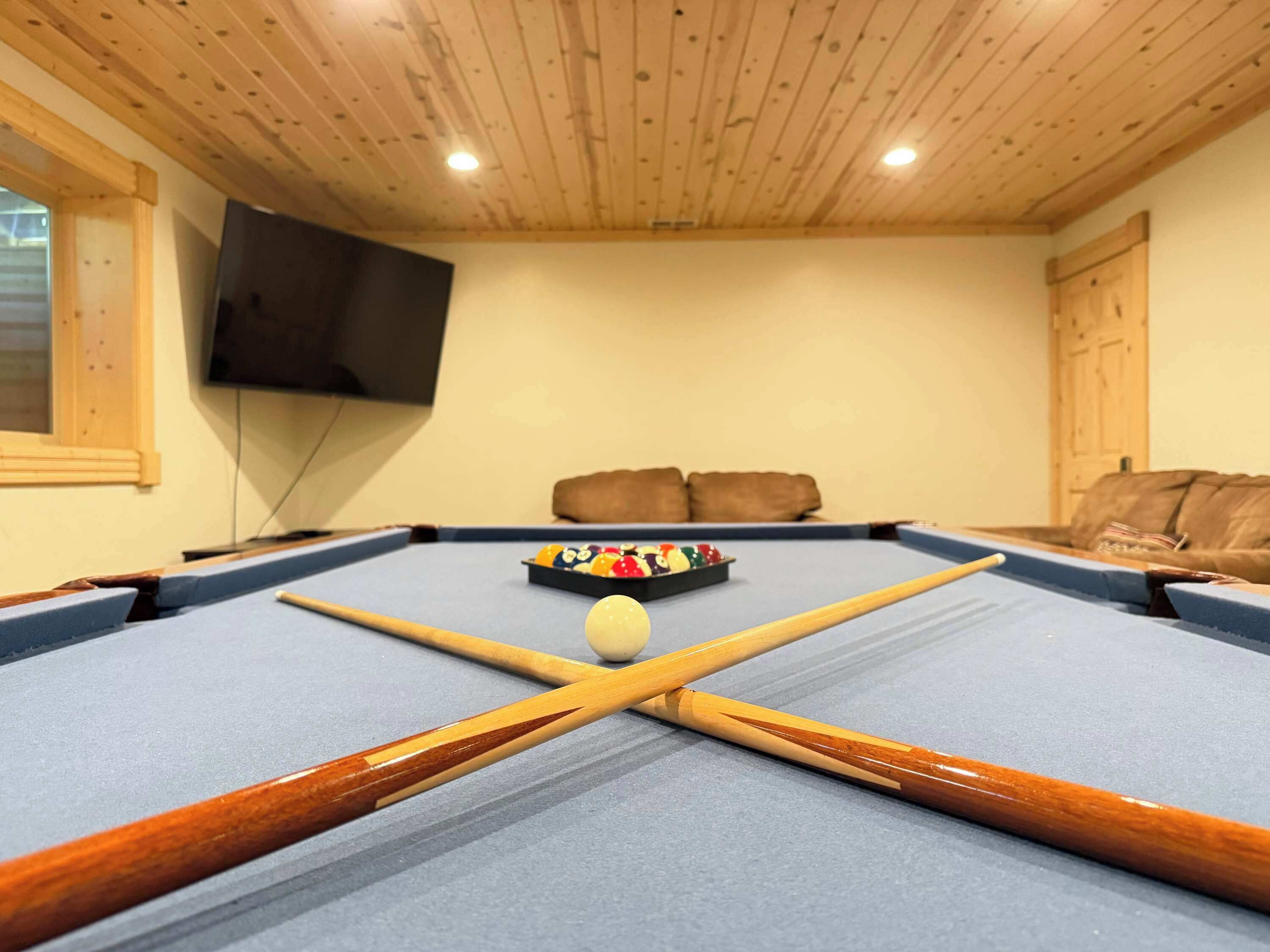A pool table with a cue stick, a billiard ball, and a set of balls in the corner.