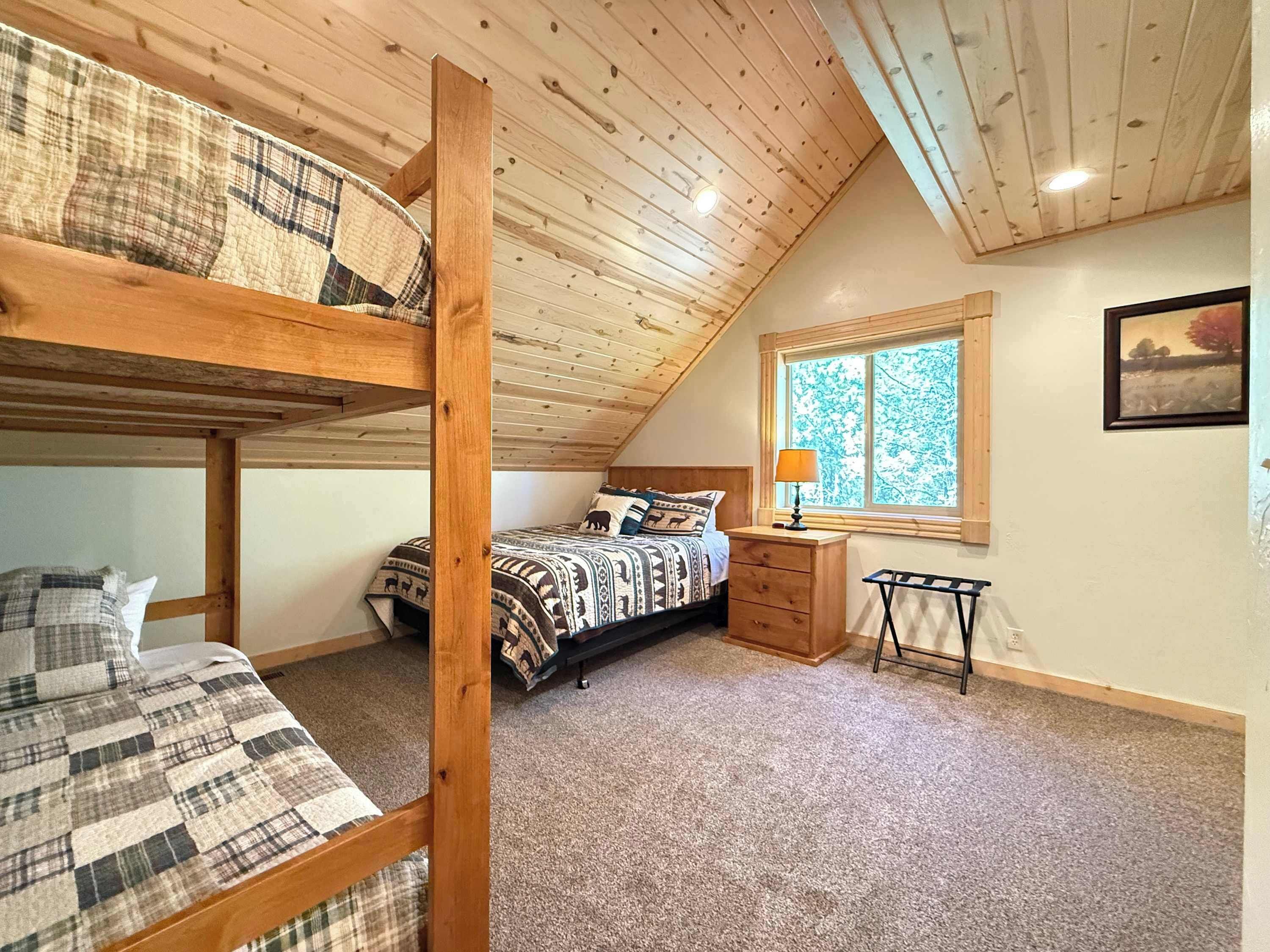 A room with a bunk bed, a single bed, a nightstand, a lamp, a window with a view, and a painting on the wall.