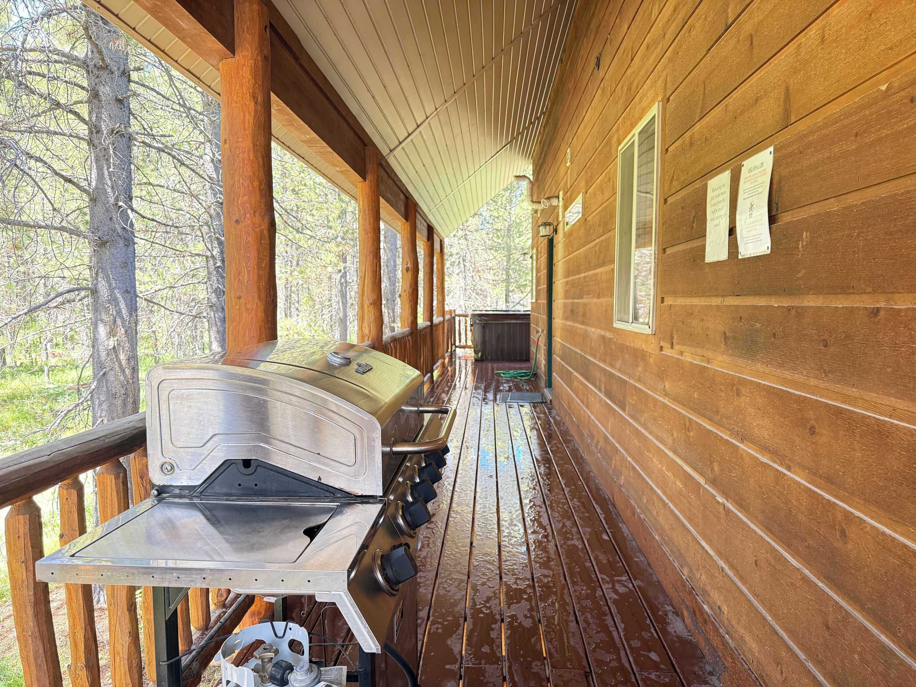 A covered wooden deck with a grill, wooden walls, and a view of trees.
