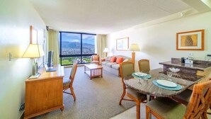 Habitación de hotel con zona de comedor, sofá, escritorio y un amplio ventanal con vistas.