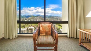 Una habitación con un ventanal grande, una silla de madera con cojín estampado y una mesita de madera.