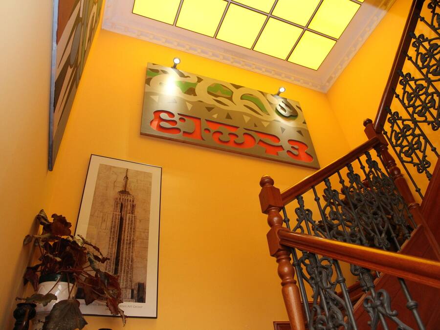 A staircase with ornate metal railings and a wooden handrail, leading to a room with a yellow wall and a framed picture.