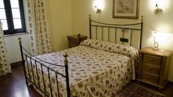A bedroom with a bed, nightstands, a window with curtains, a wall-mounted lamp, and a framed picture.