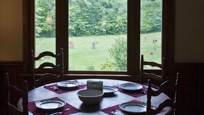 A dining table set for six with a view of a grassy area and trees through a large window. -  Restored Farmhouse 1920s.  Family and Pet Friendly. Borders National forest (Barnardsville)