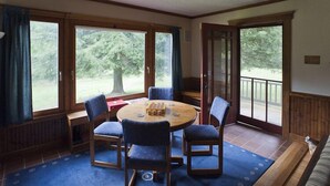 A room with a round wooden table, four chairs, a blue carpet, and large windows offering a view of trees. -  Restored Farmhouse 1920s.  Family and Pet Friendly. Borders National forest (Barnardsville)