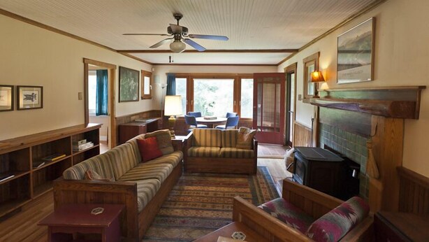 A cozy living room with a fireplace, a ceiling fan, and a large window. -  Restored Farmhouse 1920s.  Family and Pet Friendly. Borders National forest (Barnardsville)